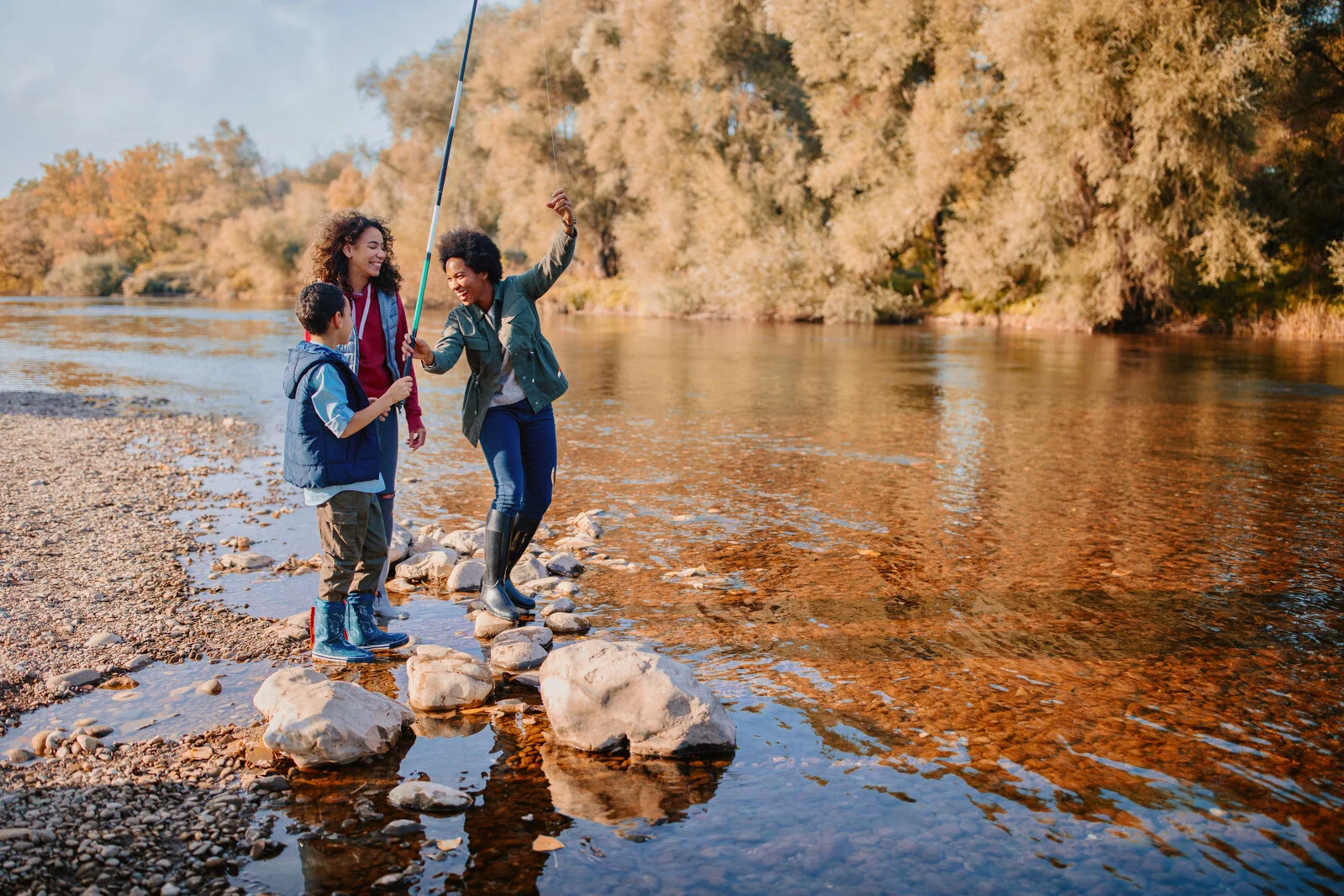 Smiling mom and two children fishing by a river